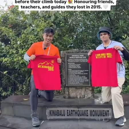 Two young men holding red shirt each standing at the memorial monument remembering those who died during the June 5, 2015 earthquake.